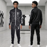 Two models wearing black tracksuits with white accents in a modern indoor setting.